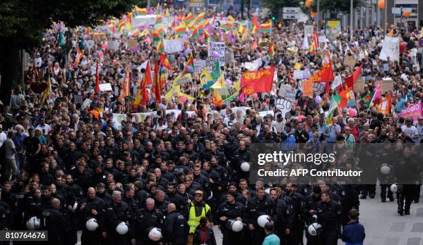 Policemen walk in front of demonstrators carrying flags and banners as they take part in the "Solidarity without borders instead of G20" on July 8,...
