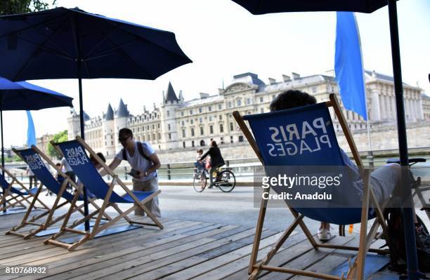 People relax under parasols on chairs, on one of the artificial Paris Plages along the River Seine during Paris Plages Days in Paris, France on July...