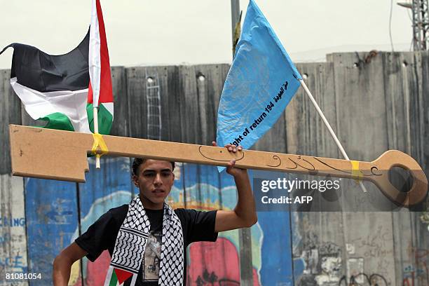 Palestinian boy holds up a large cardboard key at the head of a procession of children waving Palestinian flags as they commemorate the 60th...