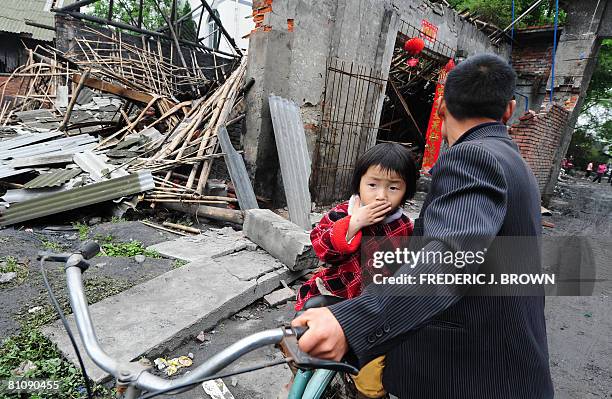 Girl covers her mouth from the smell while being pushed on a bike past the rubble behind the quake-demolished Juyuan Middle School in Juyuan on May...