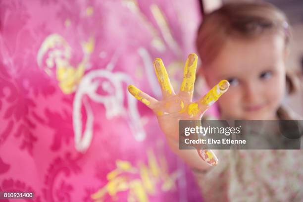 girl holding up hand covered in finger paints, next to pink wallpaper - 4 girls finger painting stock pictures, royalty-free photos & images