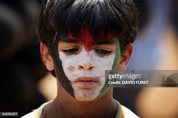 Palestinian boy with his face painted to resemble the Palestinian national flag pauses as he watches demonstrators release black balloons during a...