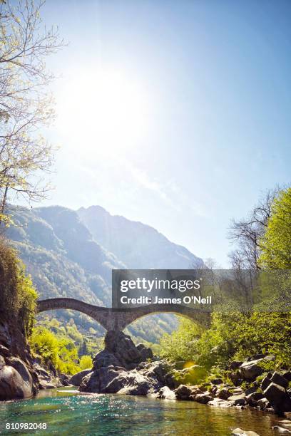 hiker crossing river on a stone bridge in switzerland - valle verzasca stock-fotos und bilder