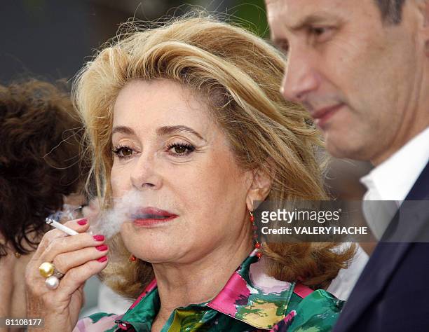 French actress Catherine Deneuve smokes a cigarette as she poses next to fellow actor Hippolyte Girardot during a photocall for French director...