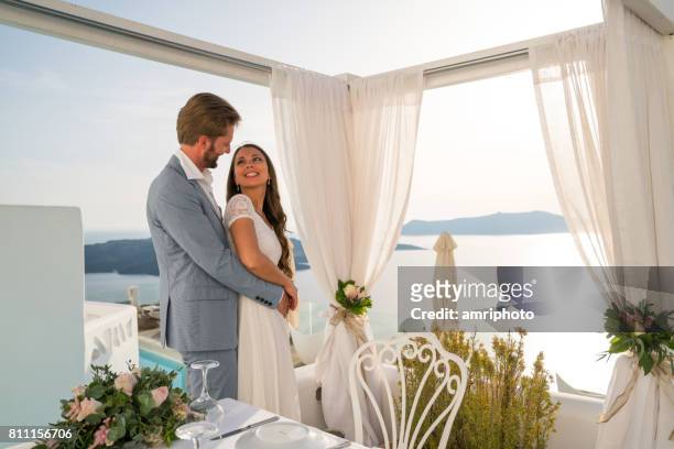 mooie bruidspaar permanent samen aan diner tafel buiten luxe restaurant in griekenland - santorini wedding stockfoto's en -beelden