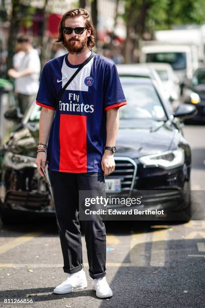 Guest wears a PSG Paris Saint Germain football soccer club "Fly Emirates" blue red and white t-hirt, black pants, sunglasses, white sneakers, outside...