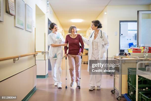 senior woman with walking stick being helped by doctor and nurse - rehabilitation center stock pictures, royalty-free photos & images