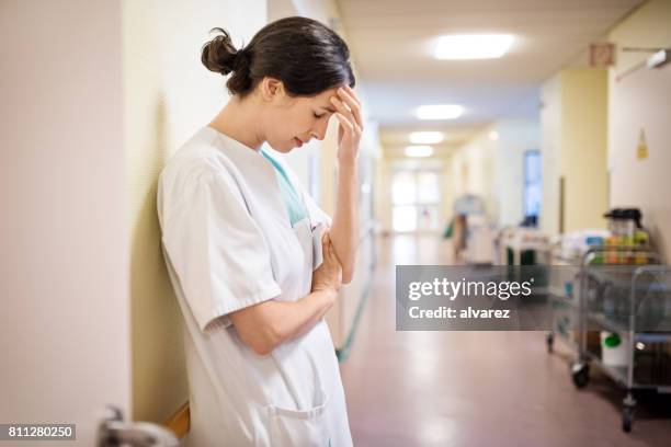 upset female nurse standing in hospital corridor - sad nurse stock pictures, royalty-free photos & images