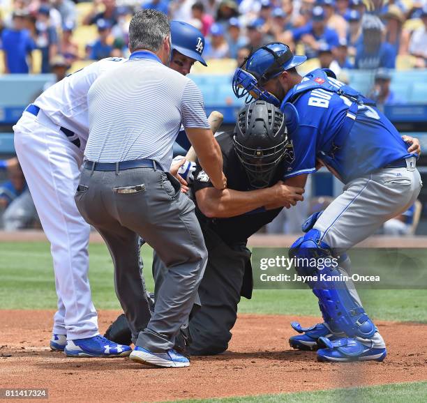 Umpire Kerwin Danley is helped by Cody Bellinger of the Los Angeles Dodgers, Drew Butera of the Kansas City Royals and team trainer Nathan Lucero,...