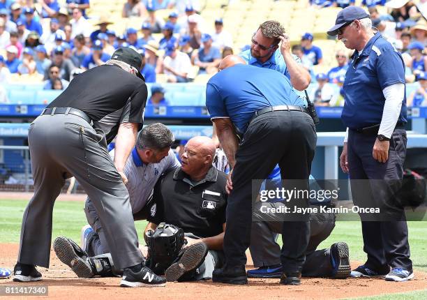 Umpire Kerwin Danley is helped by Nathan Lucero, team trainer of Los Angeles Dodgers after getting hit in the face mask in the first inning at Dodger...