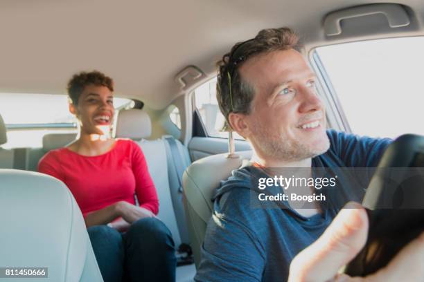 smiling male driver gives ride to smiling passenger in backseat - uber driver stock pictures, royalty-free photos & images