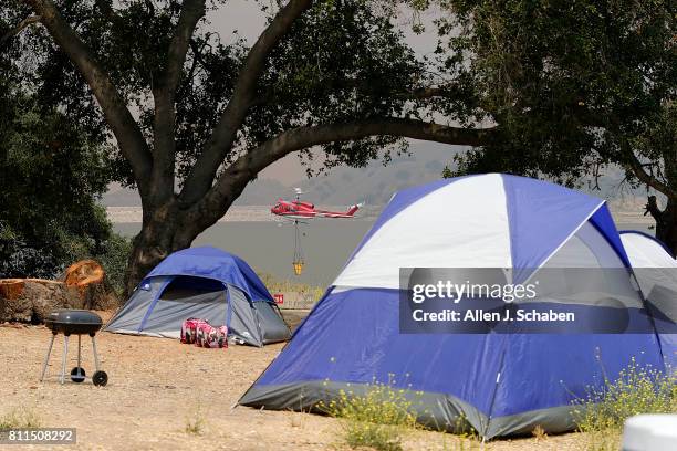Fire-fighting helicopter prepares to draw water from the lake as tents, food and personal belongs remain abandoned after campers were evacuated from...