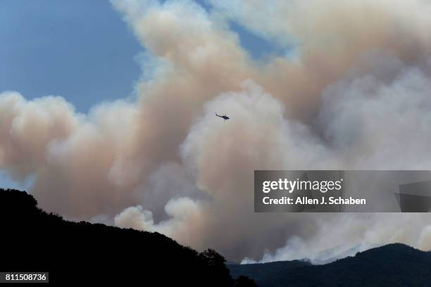 Fire-fighting helicopter gets into position to make a water drop on the Whittier Fire as it burns towards SR-154 in the Los Padres National Forest...