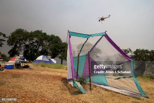 Fire-fighting helicopter passes by as tents, food and personal belongs remain abandoned after campers were evacuated from the fast-moving Whittier...