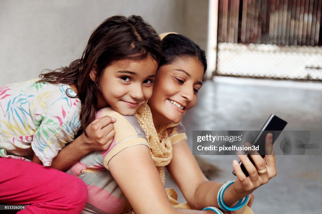 Cheerful  mother & daughter using mobile phone at home