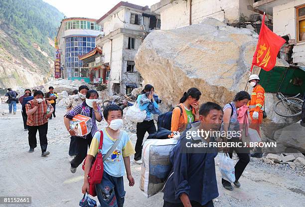 Residents flee with their belongings walking past a huge rock from landslide debris in Beichuan on May 19, 2008 in southwest China's quake-stricken...