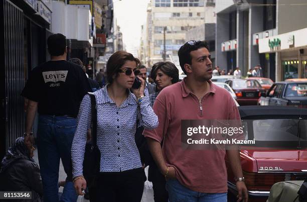 Young couple on a downtown street in Beirut, the young woman speaking into her mobile phone, 25th April 1996. A female beggar sits on the pavement...