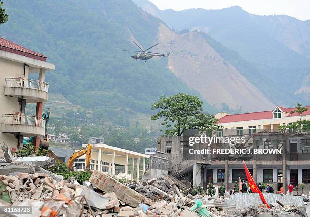 Military helicopter hovers above a search and rescue operation underway at a demolished school on the top of the hill leading to the deserted...