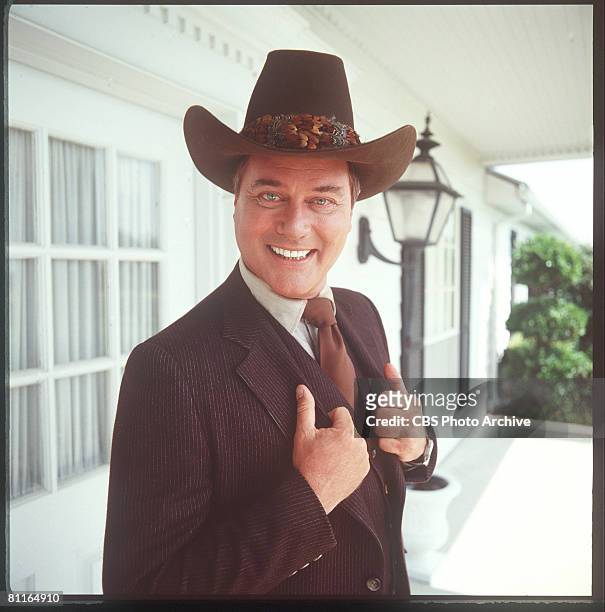 American actor Larry Hagman smiles as he holds the lapels of his pin-striped, three-piece suit, in character as John Ross 'J.R.' Ewing Jr. On the...
