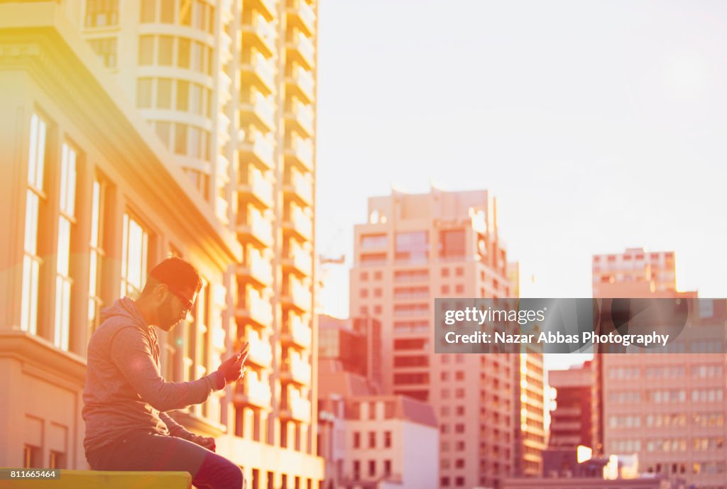 Young Man Using Smart Device With Background Of Building.