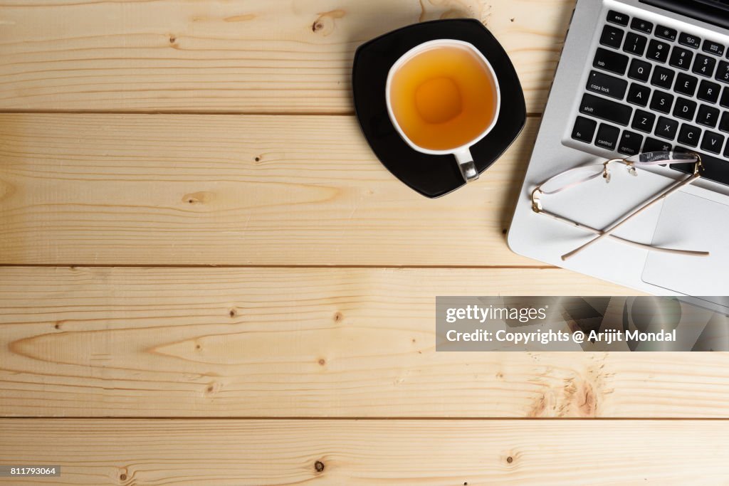 Wooden Office Table Top View with Green Tea cup, computer keyboard and spectacle