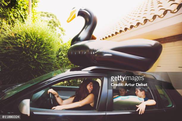 Happy family going to the beach with huge black swan on the top of the car during travel vacations in the Mediterranean sea.