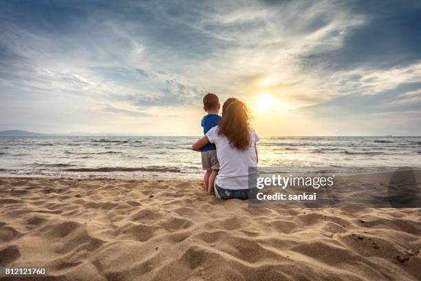 moeder met zoon genieten van de zonsondergang op het strand - mum sitting down with baby stockfoto's en -beelden