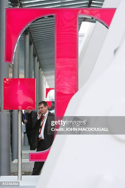 Picture taken on March 4, 2008 shows a tarde-fair visitor using his mobile phone as he walks past a logo of German telecommunications giant Deutsche...