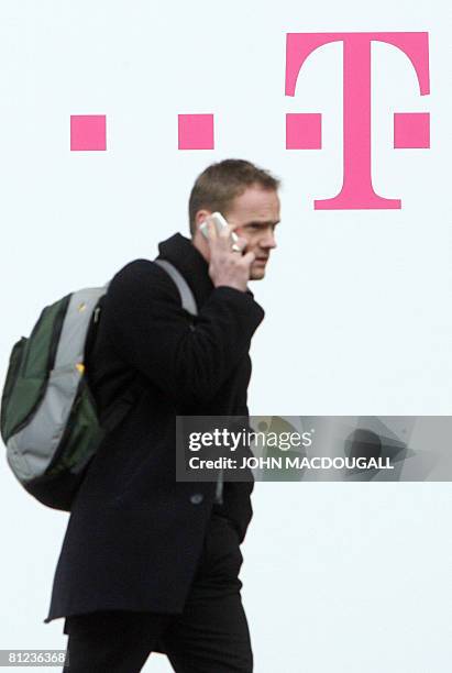 Picture taken on March 4, 2008 shows a tarde-fair visitor using his mobile phone as he walks past a logo of German telecommunications giant Deutsche...