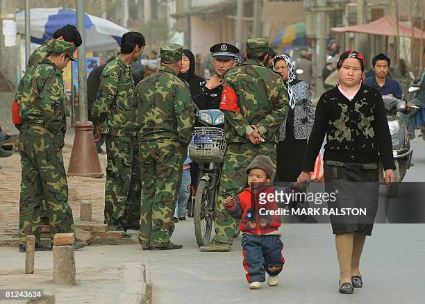 Muslim Uighur woman walks with her son past security forces in the town of Kashgar, Xinjiang Province on April 2, 2008. China has accused Muslims in...