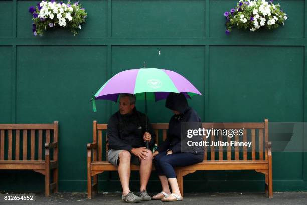 Spectators attempt to keep dry on day eight of the Wimbledon Lawn Tennis Championships at the All England Lawn Tennis and Croquet Club on July 11,...