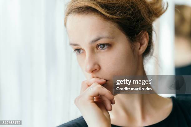 doordachte vrouw op zoek door het raam - staring stockfoto's en -beelden