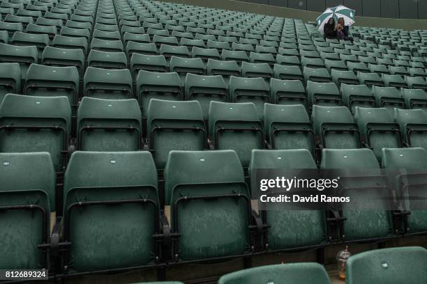 Spectators attempt to keep dry as they seat on court one on day eight of the Wimbledon Lawn Tennis Championships at the All England Lawn Tennis and...