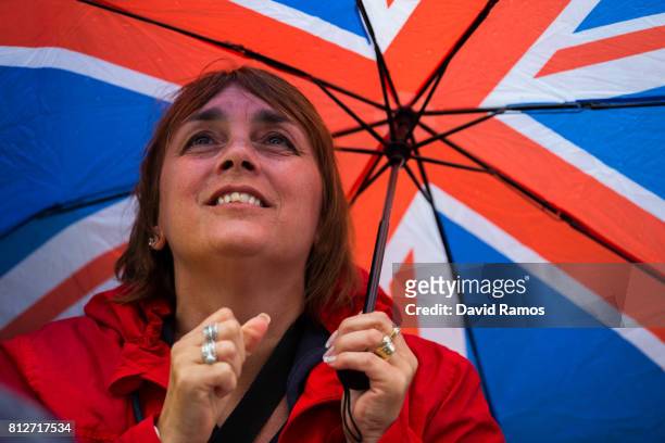 Spectator attempts to keep dry as they watch action on the screen on day eight of the Wimbledon Lawn Tennis Championships at the All England Lawn...