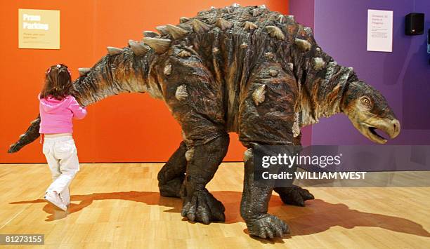 Young child inspects Minmi, a life-sized dinosaur puppet who looks surprised as it walks around an exhibition titled 'Hatching the Past: Dinosaur...