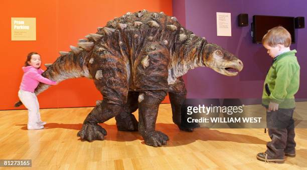 Two young children inspect Minmi, a life-sized dinosaur puppet as it walks around an exhibition titled 'Hatching the Past: Dinosaur Eggs & Babies',...