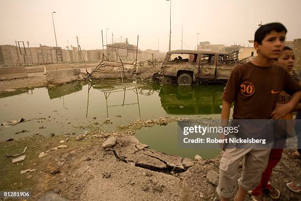 Young boys living in Sadr City at a concrete wall recently erected by American forces look over destroyed and burned vehicles from heavy fighting...