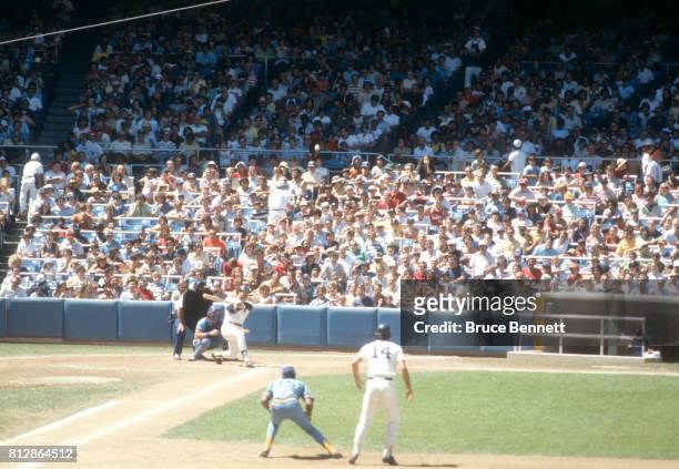 Reggie Jackson of the New York Yankees swings at the pitch as teammate Lou Piniella takes a lead as first baseman Cecil Cooper of the Milwaukee...