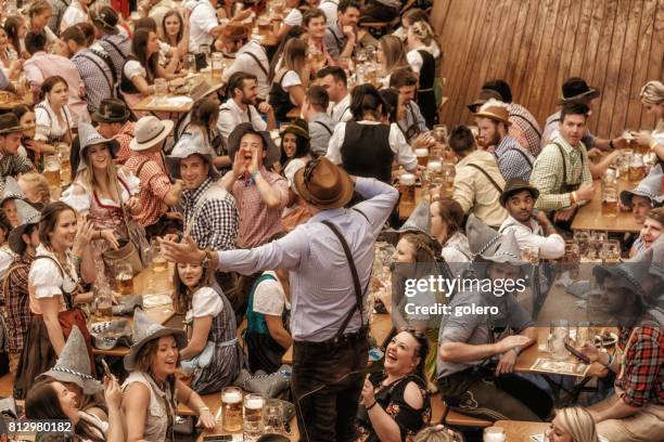 young people celebrating in beer pavilion on oktoberfestfest in munich - oktoberfest party stock pictures, royalty-free photos & images