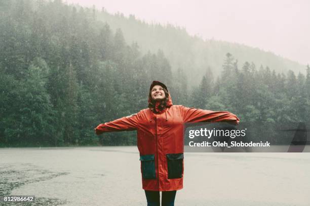 frau im regenmantel stand in der nähe des sees bei strömendem regen - wandern regen stock-fotos und bilder