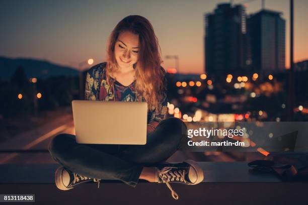 tienermeisje met behulp van laptop door de nacht tegen de stedelijke skyline - the study of pose opening night stockfoto's en -beelden