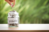 Hand putting Coins in glass jar for giving and donation concept