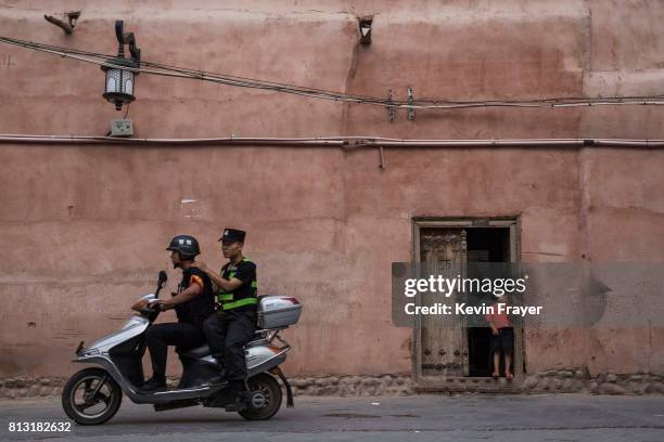Police patrol on a scooter as an ethnic Uyghur boy stands in his doorway on June 27, 2017 in the old town of Kashgar, in the far western Xinjiang...