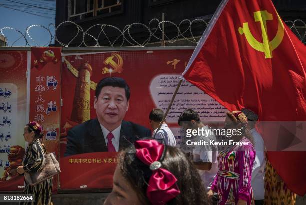 Ethnic Uyghur members of the Communist Party of China carry a flag past a billboard of Chinese President Xi Jinping as they take part in an organized...
