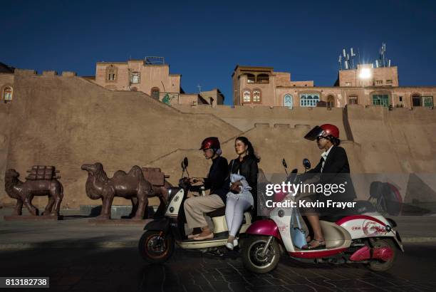 Ethnic Uyghurs ride by a newly finished section of the old city walls on June 30, 2017 in the old town of Kashgar, in the far western Xinjiang...