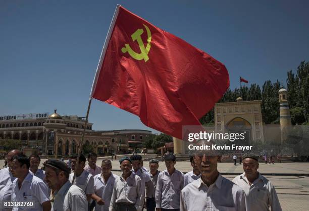 Ethnic Uyghur members of the Communist Party of China carry a flag as they take part in an organized tour outside Id Kah Mosque on June 30, 2017 in...