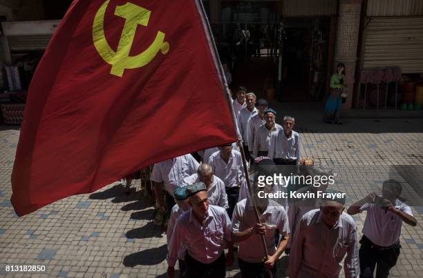 Ethnic Uyghur members of the Communist Party of China carry a flag as they take part in an organized tour on June 30, 2017 in the old town of...