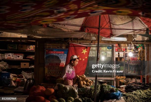 An ethnic Uyghur shopkeeper works next to a Chinese flag at his shop on June 29, 2017 in the old town of Kashgar, in the far western Xinjiang...