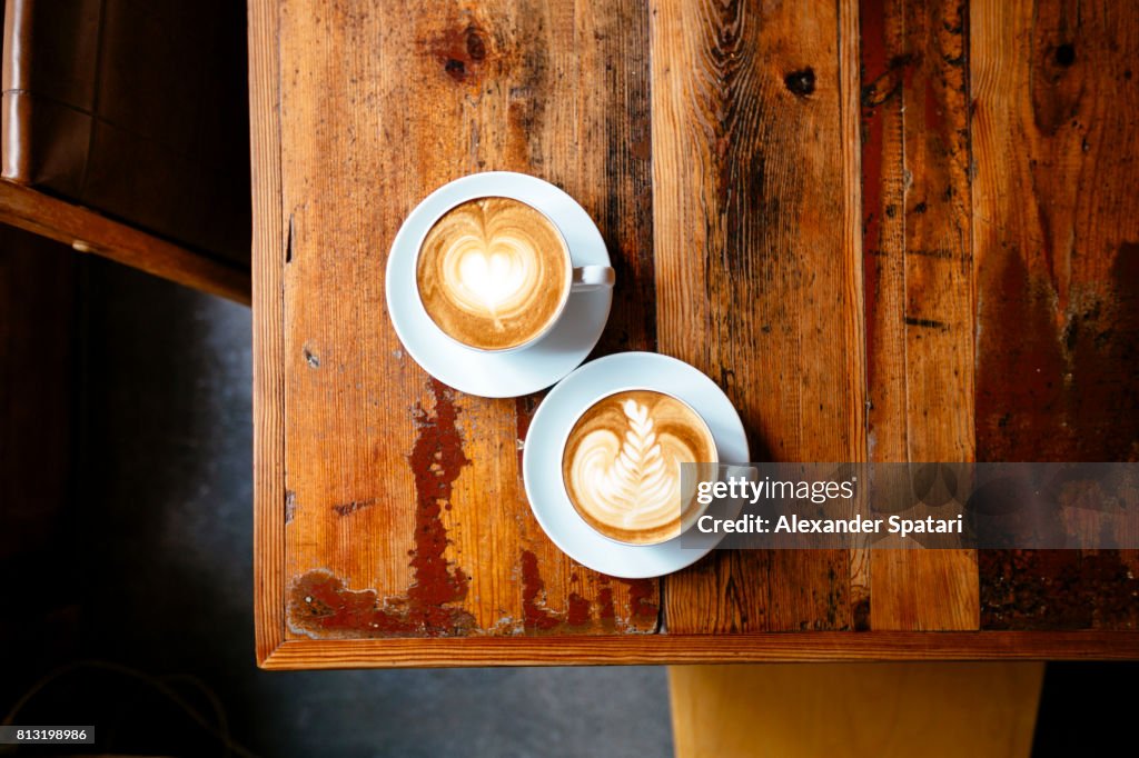 Two cups of coffee with foam latte art on a wooden table seen from above