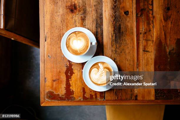 two cups of coffee with foam latte art on a wooden table seen from above - table romantique photos et images de collection